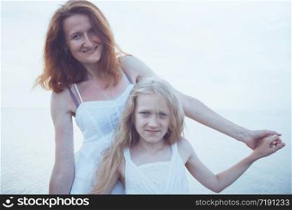 happy family weekend by the sea - Mom and daughter in white dresses walking by the sea at sunset. Ukrainian landscape at the Sea of Azov, Ukraine