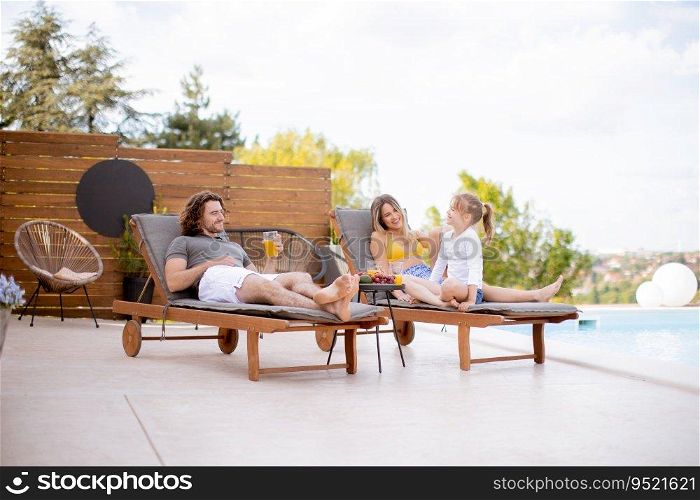 Happy family with a mother, father and daughter sitting on the deck chairs by the swimming pool
