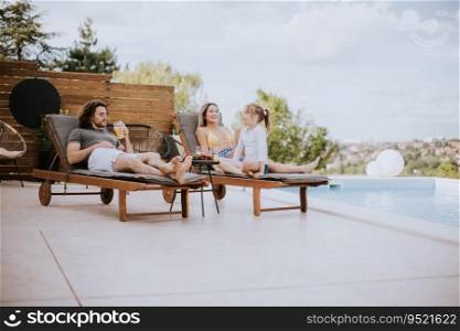 Happy family with a mother, father and daughter sitting on the deck chairs by the swimming pool