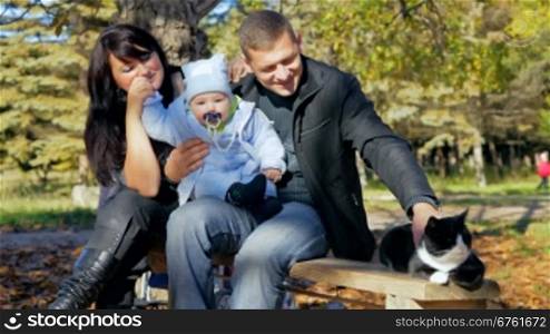 happy family with a toddler and a cat resting on a bench in the park