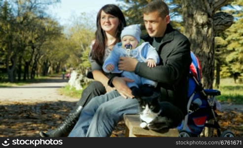 happy family with a toddler and a pet resting on a bench in the park