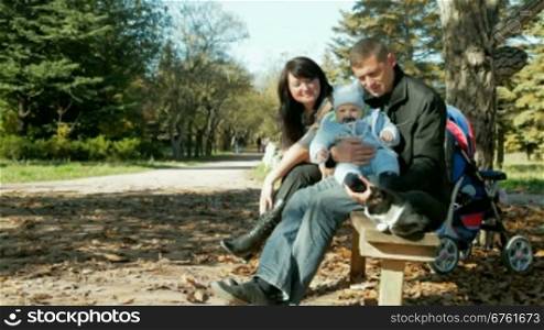 happy family with a toddler and a pet resting on a bench in the park