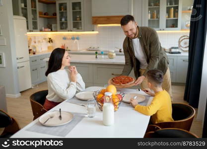 Happy family with child eating pizza sitting at dining table. Caring father cooked food for lunch. Happy family with child eating pizza sitting at dining table