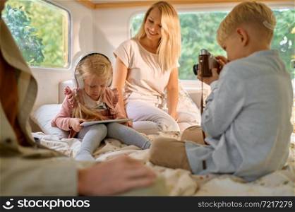 Happy family with kids relaxing in motorhome, summer camping. Couple with children travel in camp car, trailer interior on background. Campsite adventure, travelling lifestyle, vacation on rv car. Family with kids relaxing in motorhome, camping