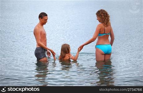 Happy family with little girl bathe in sea, standing back