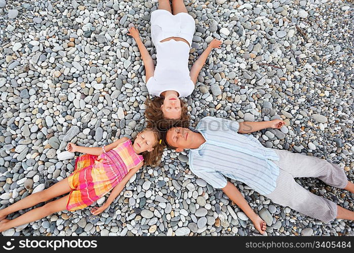 Happy family with little girl lying on stony beach, closed eyes, Concerning with heads