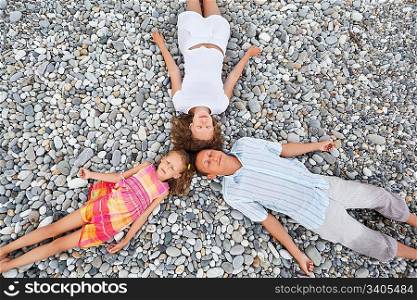 Happy family with little girl lying on stony beach, closed eyes, Concerning with heads