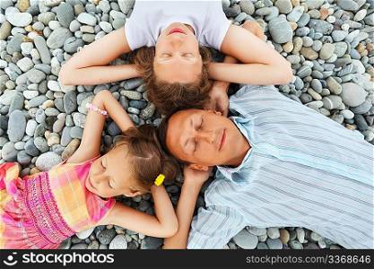 Happy family with little girl lying on stony beach, Concerning with heads, holding hands behind head