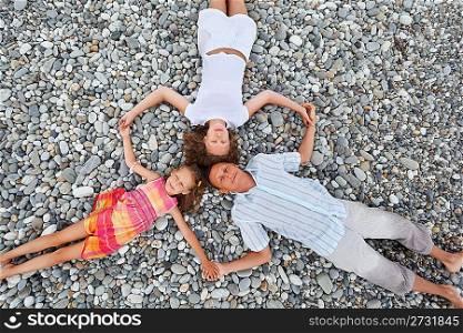 Happy family with little girl lying on stony beach, having joined hands, Concerning with heads