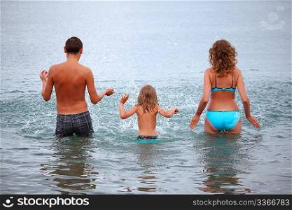Happy family with little girl splashes water hands standing on belt in sea, standing back