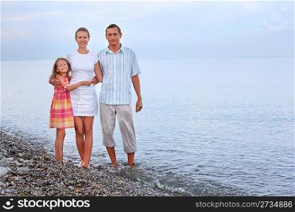 Happy family with little girl standing on beach in evening