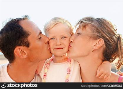 Happy family with little near to sea, parents kiss daughter