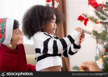 Happy family with mother and daughter decorating ornament on Christmas tree together at home, thanksgiving eve, celebration of woman and child bonding in Christmas day, enjoyment and fun on holiday.
