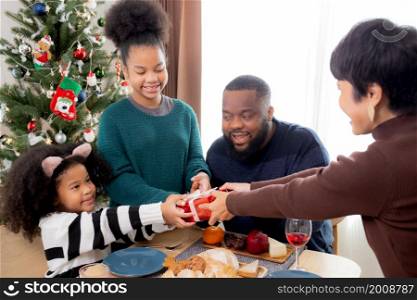 Happy family with mother giving gift box with daughter during dinner at home, celebration in xmas with parent surprising children with enjoyment at house, thanksgiving eve, Merry Christmas.