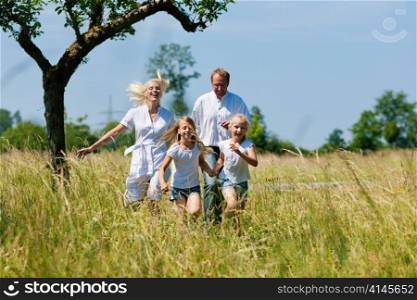 Happy Family with two girls running in a meadow in summer