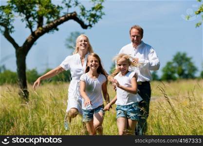 Happy Family with two girls running in a meadow in summer