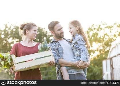 Happy family with vegetables in crate talking at farm against sky