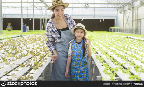 Happy farmer mom and daughter working in hydroponic greenhouse farm, clean food and healthy eating concept