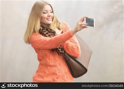Happy fashion woman in park taking selfie photo.. Happy fashion woman in fall autumn park taking selfie self photo picture. Pretty joyful young girl in sweater pullover with handbag photographing.