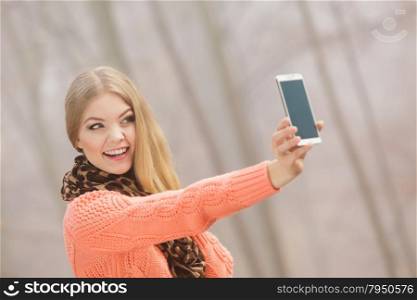 Happy fashion woman in park taking selfie photo.. Happy fashion woman in fall autumn park taking selfie self photo picture. Pretty joyful young girl in sweater pullover photographing.