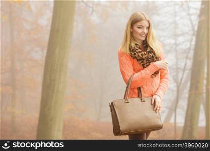 Happy fashion woman with handbag in autumn park. Happy fashionable woman in foggy autumn park. Pretty young girl with handbag in forest. Fall fashion vogue.