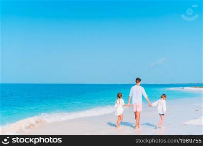 Happy father and adorable little kids on tropical beach having fun. Family vacation. Happy father and his adorable little daughters at tropical beach having fun