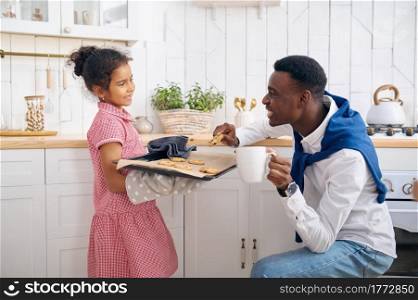 Happy father and daughter eats fresh cakes on breakfast. Smiling family eats on the kitchen in the morning. Dad feeds female child, good relationship. Father and daughter eats fresh cakes on breakfast