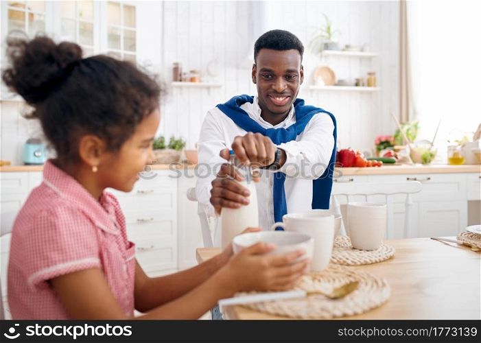Happy father and daughter having breakfast at home. Smiling family eats on the kitchen in the morning. Dad feeds female child, good relationship. Father and daughter having breakfast at home