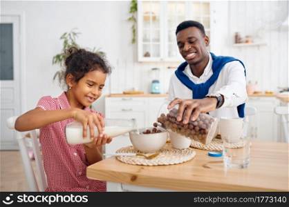 Happy father and daughter having breakfast at home. Smiling family eats on the kitchen in the morning. Dad feeds female child, good relationship. Father and daughter having breakfast at home