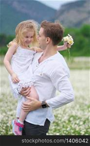 Happy father and daughter in big camomile mountain meadow. Emotional, love and care scene.