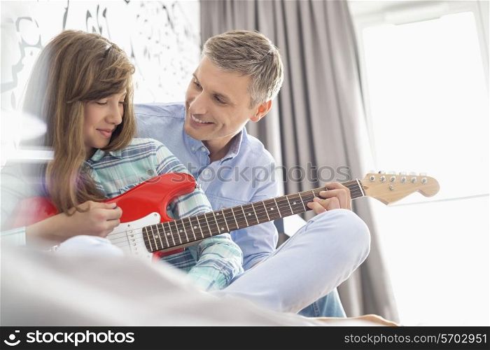 Happy father and daughter playing electric guitar at home