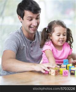 Happy father and daughter playing with building blocks at table in house