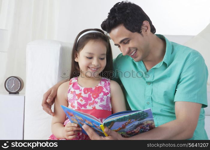 Happy father and daughter reading story book on sofa at home
