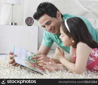 Happy father and daughter reading story book while lying on rug at home