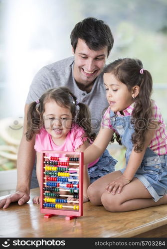 Happy father and daughters playing with abacus in house