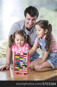 Happy father and daughters playing with abacus in house