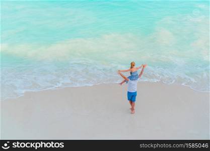 Happy father and his adorable little daughter at white sandy beach from above view. Little girl and happy dad having fun during beach vacation