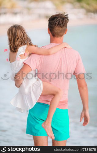 Happy father and his adorable little daughter at white sandy beach walk and talk. Little girl and happy dad having fun during beach vacation