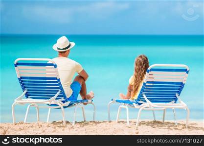 Happy father and his adorable little daughter on the beach relax on the loungers. Little girl and happy dad having fun during beach vacation
