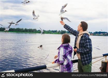 Happy father and little girl feed seagulls on the river. Happy father and little girl feed seagulls
