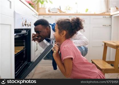 Happy father and little kid cooking cakes in oven on breakfast. Smiling family on the kitchen in the morning. Dad feeds female child, good relationship. Father and kid cooking cakes in oven on breakfast