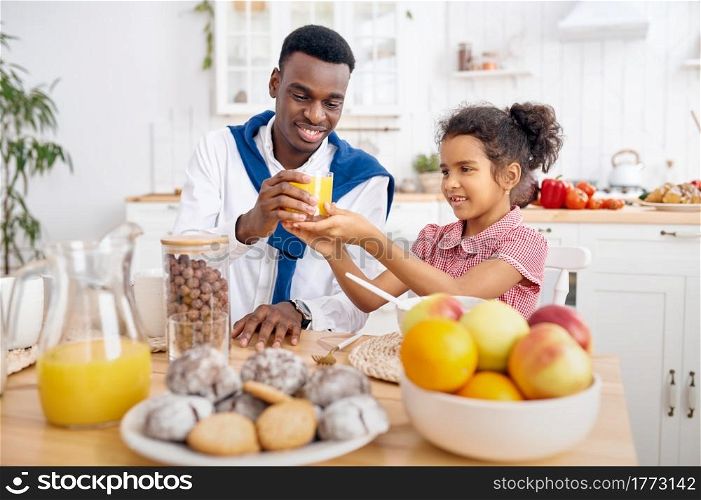 Happy father and little kid drinks fresh juice on breakfast. Smiling family eats on the kitchen in the morning. Dad feeds female child, good relationship. Father and kid drinks fresh juice on breakfast