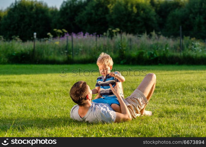 Happy father and son having fun outdoor on meadow. Happy man and child having fun outdoor on meadow. Family lifestyle scene of father and son resting together on green grass in the park.