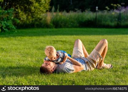 Happy father and son having fun outdoor on meadow. Happy man and child having fun outdoor on meadow. Family lifestyle scene of father and son resting together on green grass in the park.