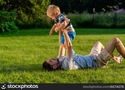 Happy father and son having fun outdoor on meadow. Happy man and child having fun outdoor on meadow. Family lifestyle scene of father and son resting together on green grass in the park.