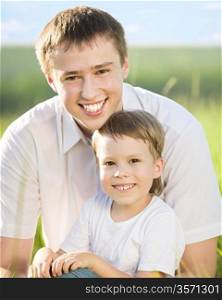 Happy father and son having fun outdoors in spring green field against blue sky background