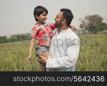 Happy father and son looking at each other with wheat field in background