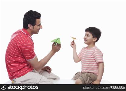 Happy father and son playing with paper airplane against white background