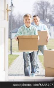 Happy father and son with cardboard boxes entering new home