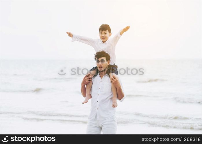 Happy father carrying his son on the neck on a tropical sand beach in summer.